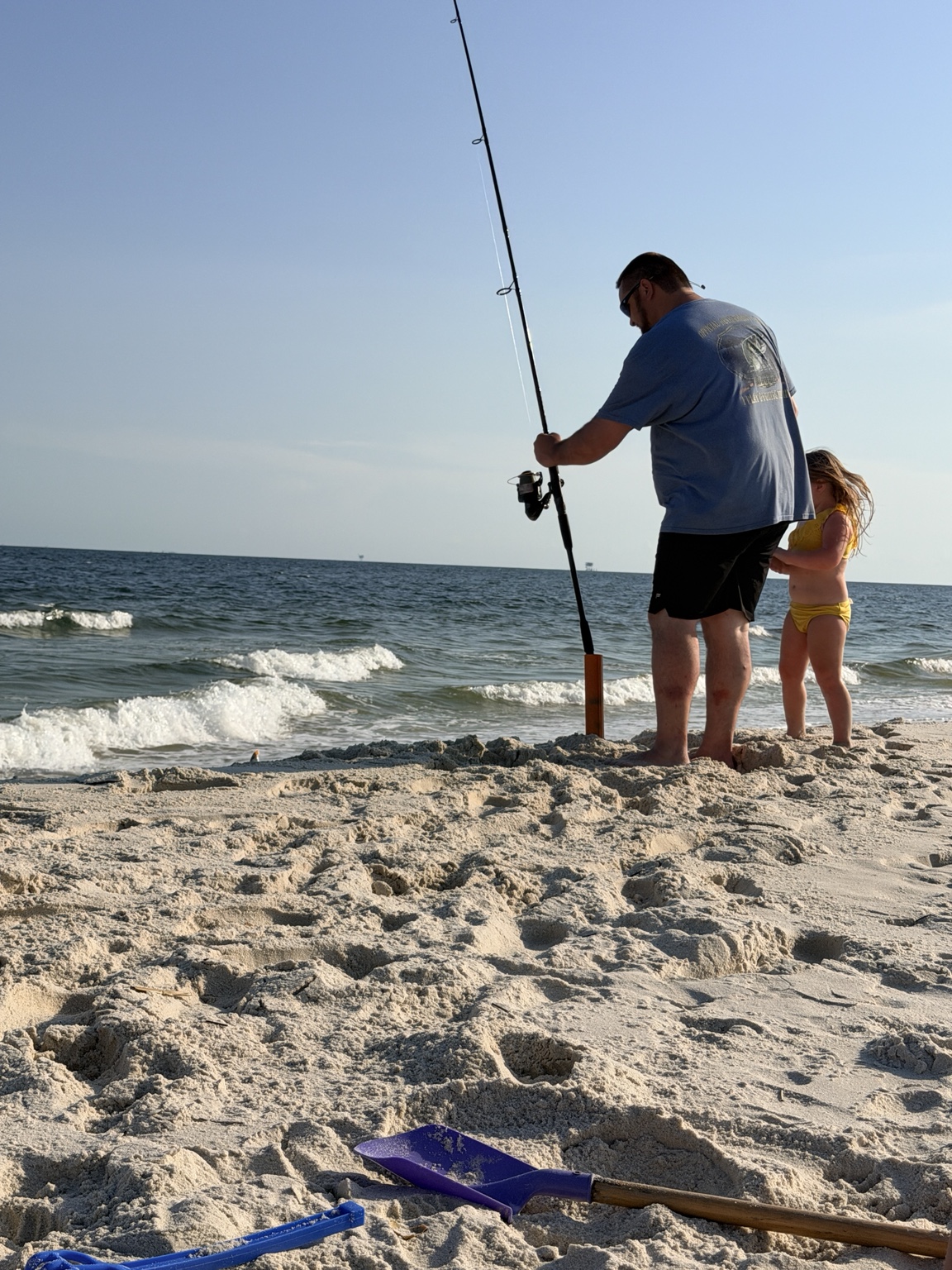 Father and daughter tending a surf-fishing rod at the waterline