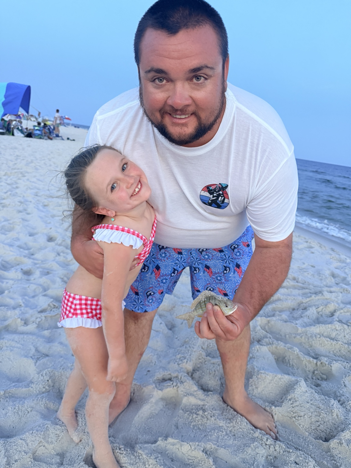Father and daughter smiling together with a fish on the beach