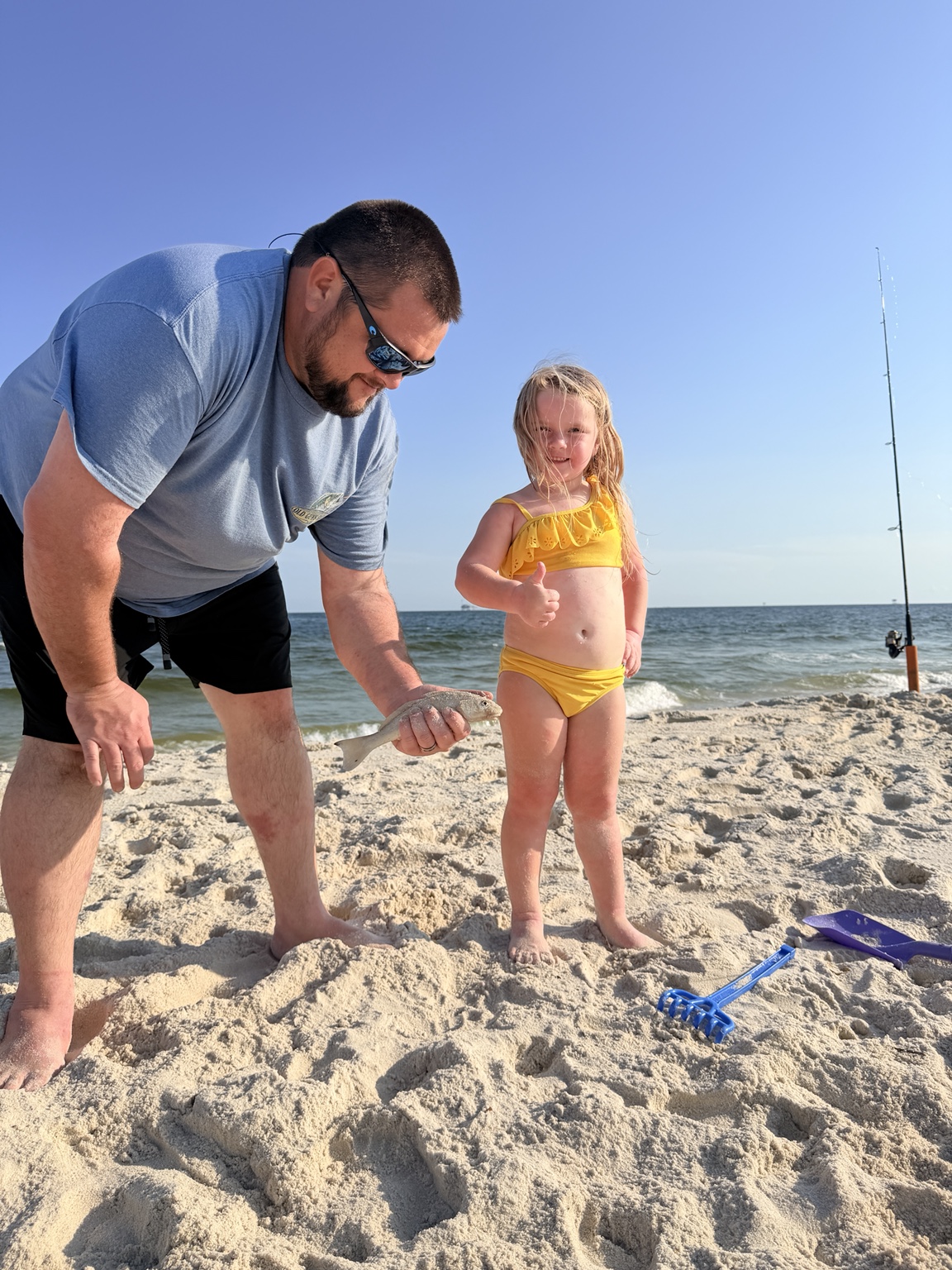 Young girl giving a thumbs-up beside her father and a beach catch