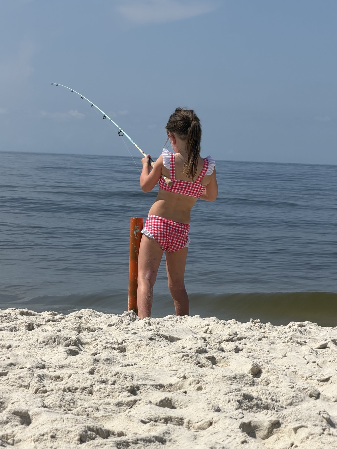 Young girl fighting a fish from the beach with a bent rod