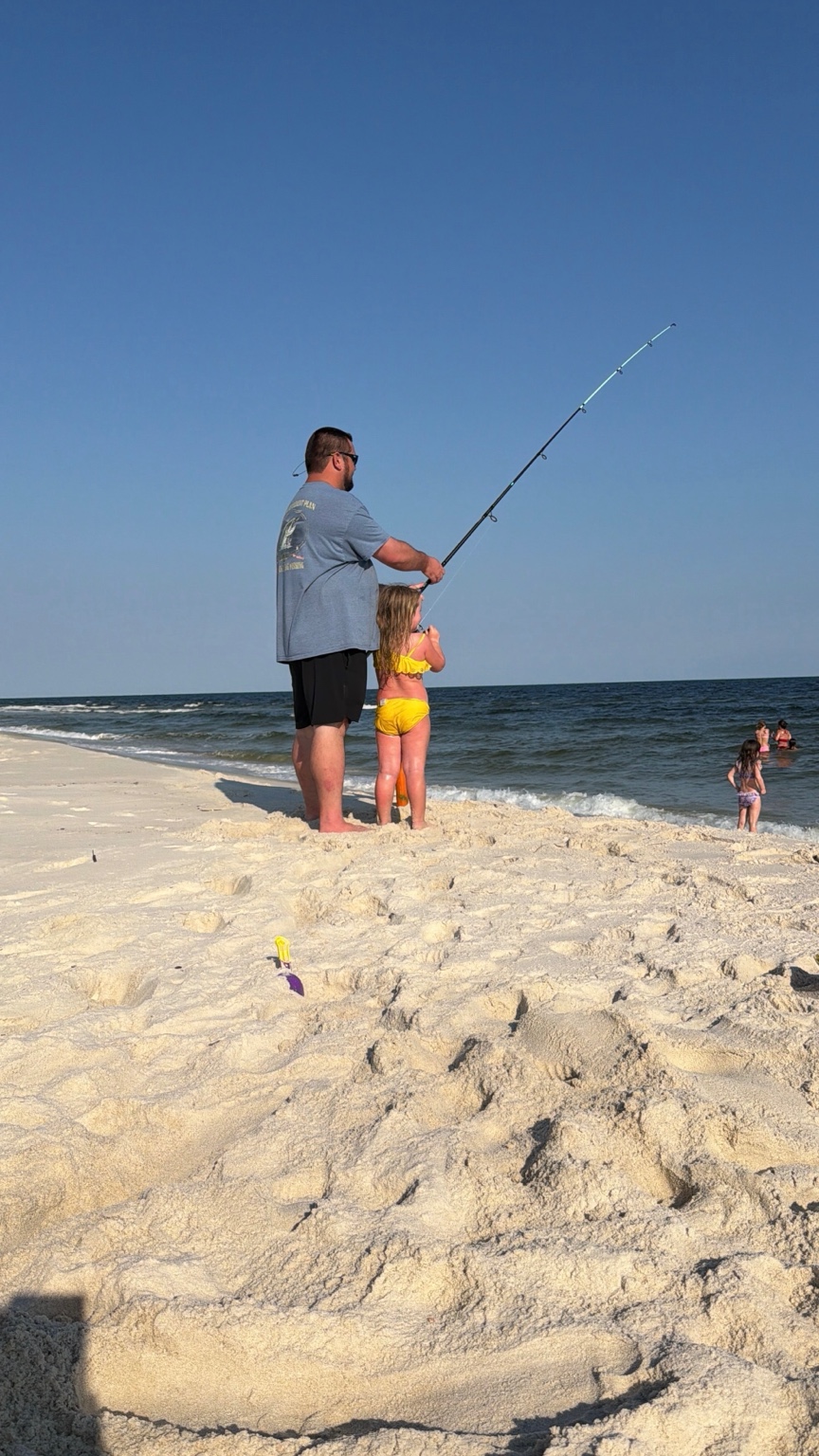 Father helping his daughter surf fish from the beach